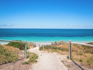 A coastal path leading to a beach with clear blue water, surrounded by vegetation and a metal railing. - Wake up to ocean views and wander barefoot across to the beach for a morning swim, coffee or sunset walk along the shoreline  Perfect for families, couples or work trips, the home offers (Safety Bay)