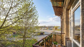 A balcony with a view of a city street, a wooden railing, and a window.