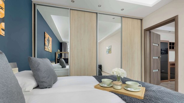 A modern bedroom with a large bed, a wooden bedside table, a sliding door closet, and a skylight.
