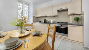 A modern kitchen with light-colored cabinets, a built-in oven, and a dining area with a wooden table set for two.