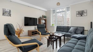 A modern living room with a sofa, two armchairs, a coffee table, a TV, and a bookshelf.