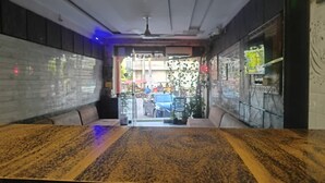 En restaurantindretning med et langt bord, polstrede siddepladser, en ventilator i loftet og udsigt til gaden gennem glasdøren.