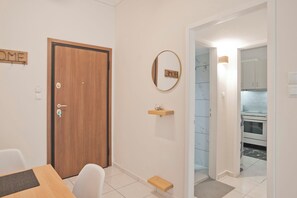 A room with a wooden door, a mirror, a small shelf with a bowl, and a view into a kitchen area. - Urban Muse Exarchia (Athina)