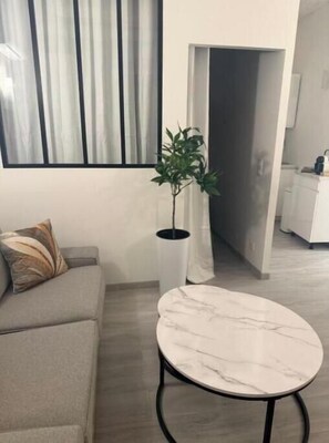 Ein Wohnzimmer mit einer Couch, einem Marmortisch, einer Topfpflanze und Blick auf eine Küche durch einen offenen Durchgang.