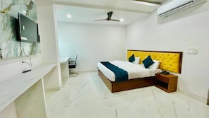 A bedroom with a bed, bedside table, TV, and ceiling fan. - sai sansthan inn (Lucknow)
