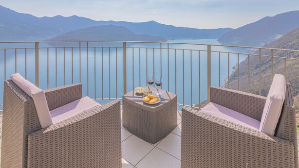 Un balcón con mobiliario de mimbre, una mesa con un plato de comida y vasos, y una vista panorámica de la montaña.