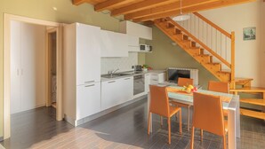Una cocina moderna con armarios blancos, una zona de comedor con sillas naranjas y una escalera de madera.