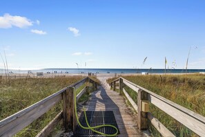 A wooden boardwalk leading to a beach with a drainpipe on it.