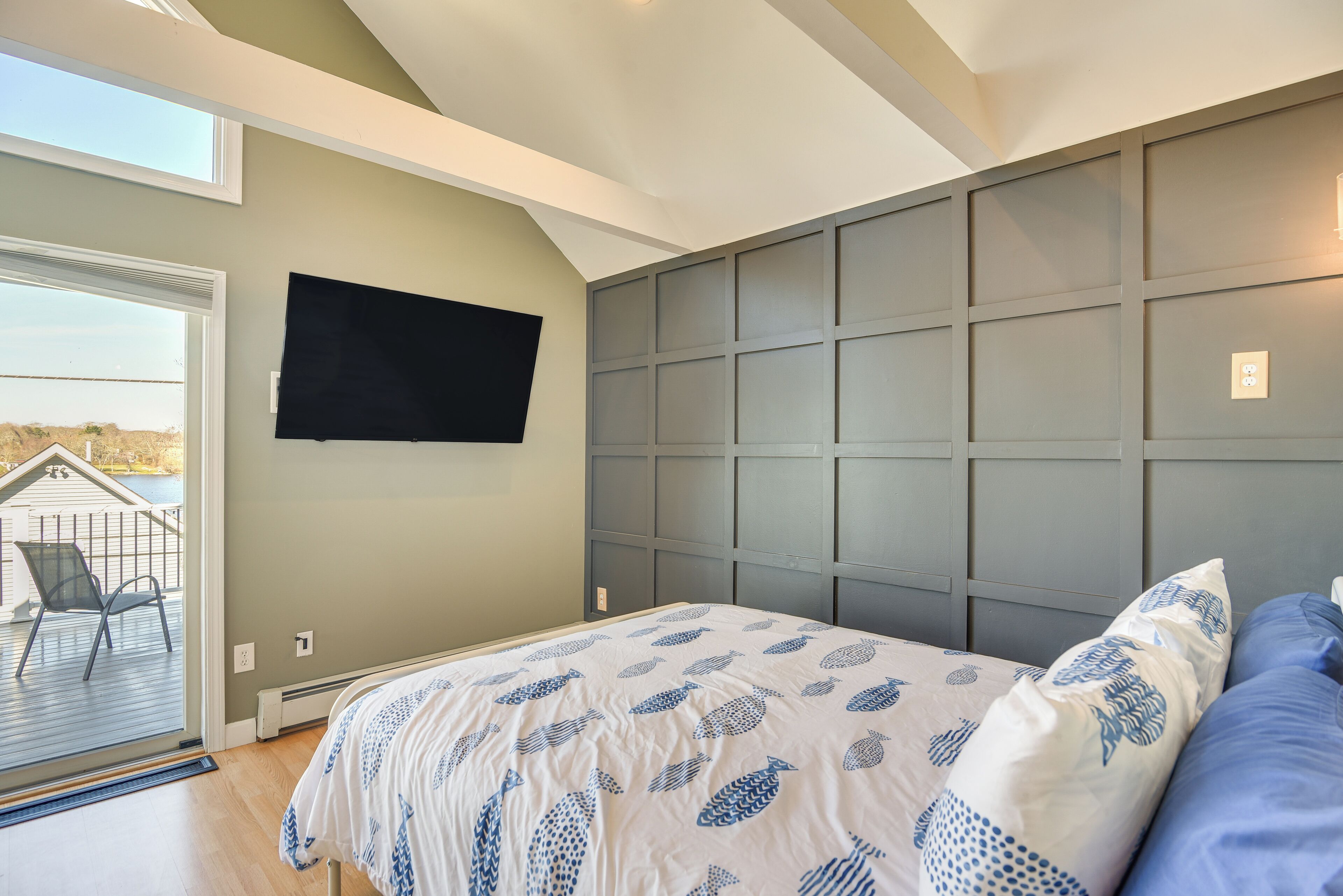 Ein Schlafzimmer mit einem Bett, einem an der Wand befestigten Fernseher und Blick ins Freie durch eine Schiebetür.