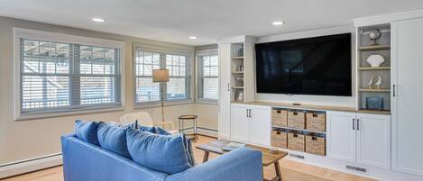 A living room with a blue sofa, a TV, white cabinets, and a large window.