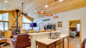 A cozy cabin interior with a fireplace, wooden ceiling, a kitchen area, and a living room with a leather couch. - Escape to Alpine! Outstanding Cabin w/ Deck & Yard (Alpine)