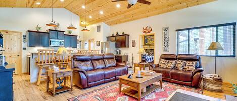 A spacious living area with a ceiling fan, wooden flooring, and a large window.