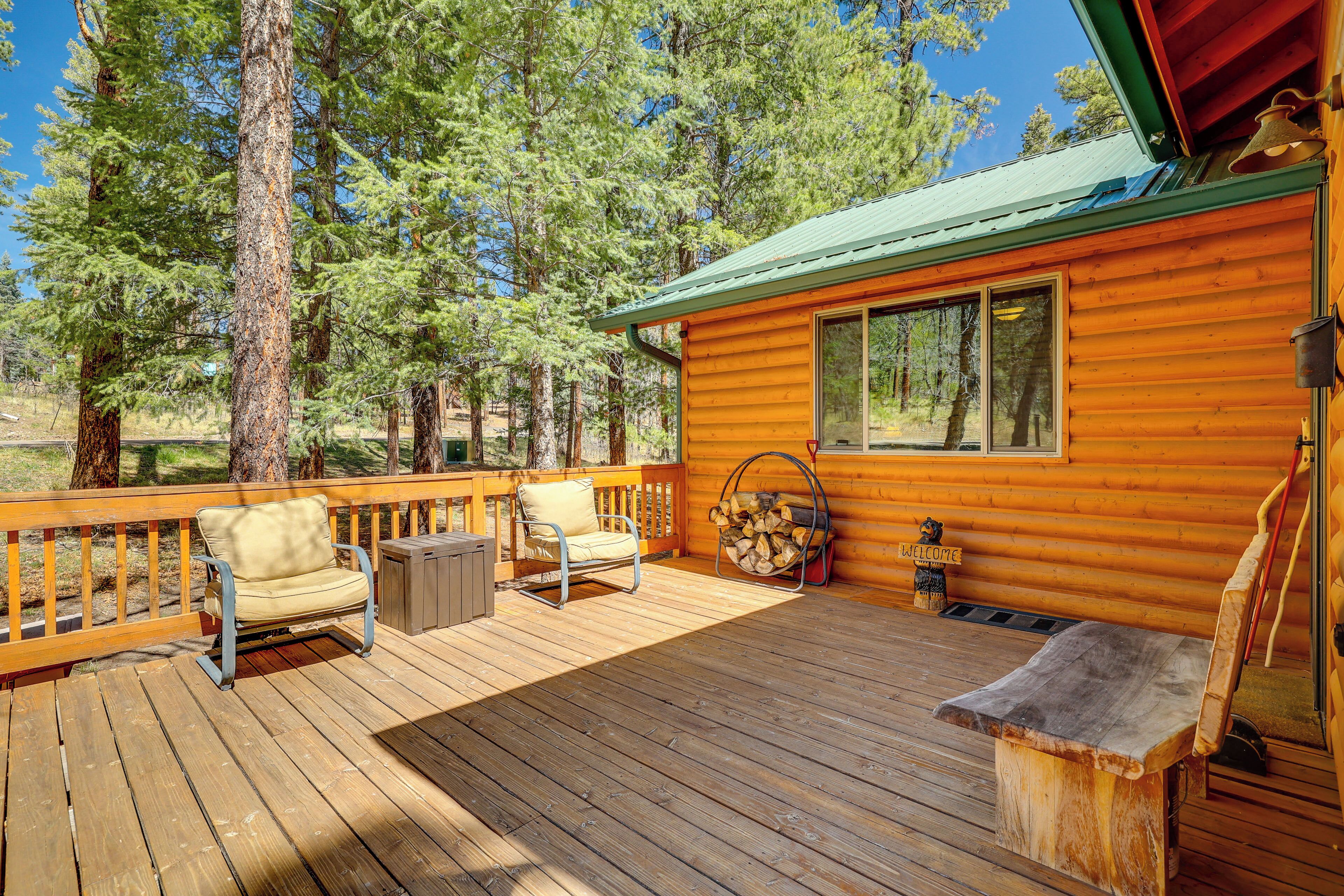 A wooden cabin with a deck, a bench, a chair, and a welcome sign.