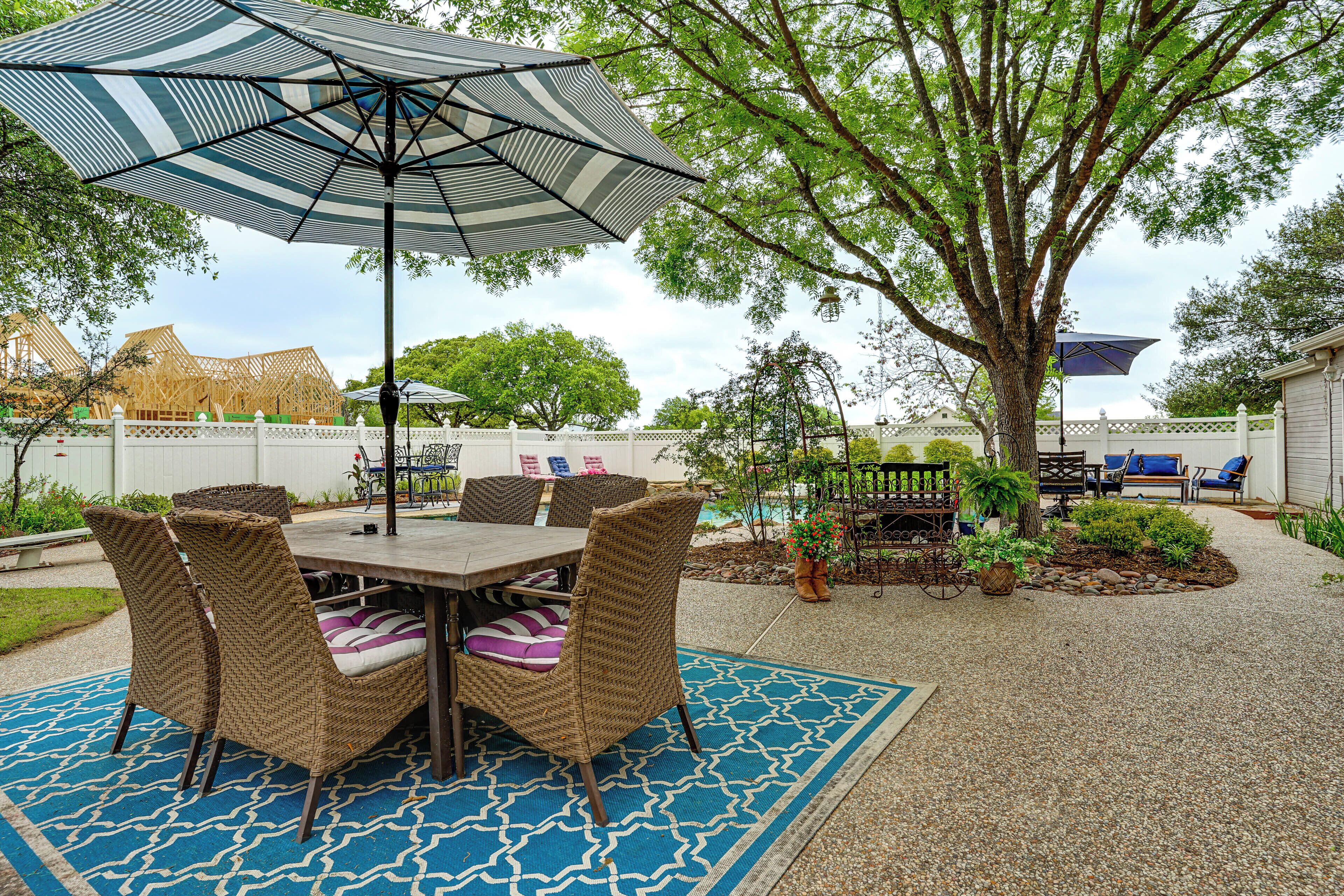 A patio with a table and chairs, a large umbrella, and a tree.
