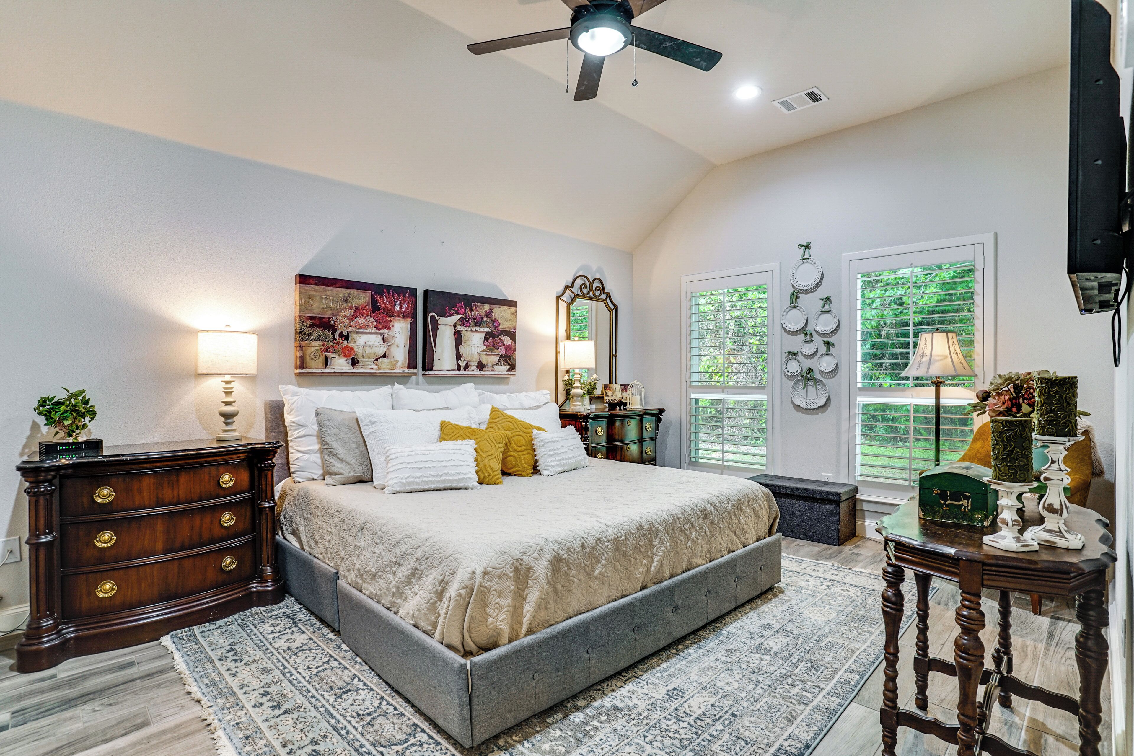 A bedroom with a bed, dresser, nightstand, lamp, and decorative items.
