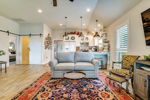 A living room with a sofa, a patterned rug, a dining area with a chair, and a kitchen in the background.