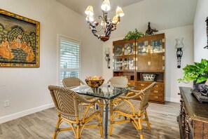 A dining area with wicker chairs, a glass-top table, a chandelier, a wooden cabinet with glass doors, and a wall-mounted lamp. - Backyard Bungalow w/ Pool & Country Views (Argyle)