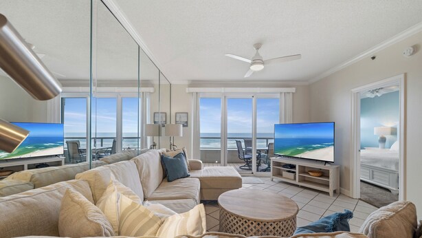 A spacious living room with a large sofa, a coffee table, and a flat-screen TV. There are large windows offering a view of the ocean. - The Enclave 403 by Liquid Life (Orange Beach)