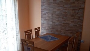 Een eetruimte met een houten tafel en stoelen, een klok aan de muur, en een schilderij boven de tafel.