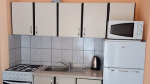 Een keuken met witte kastjes, een fornuis, een magnetron en een koelkast.