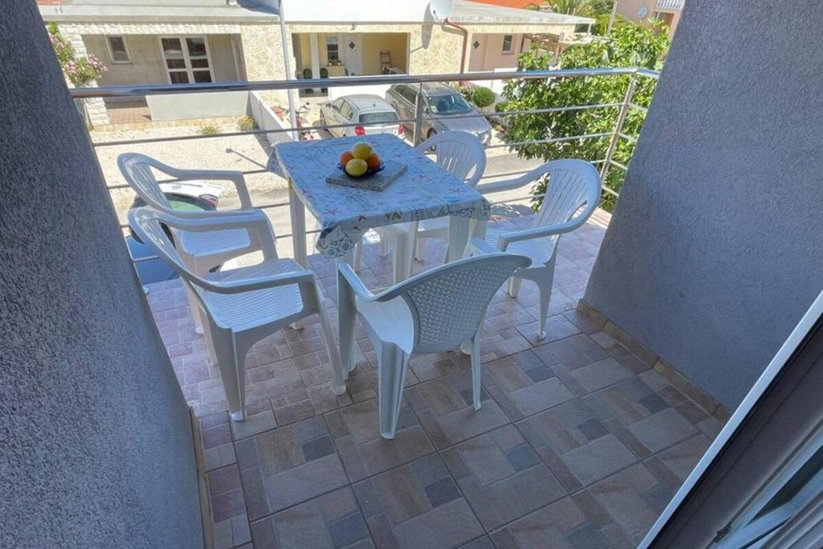 A balcony with a table and chairs, a small table with fruit, and a view of the street.