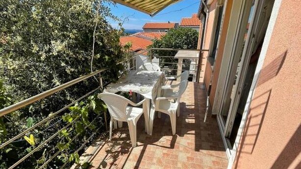 Een balkon met een betegelde vloer, witte plastic stoelen, een tafel en een gestreept zonnescherm.