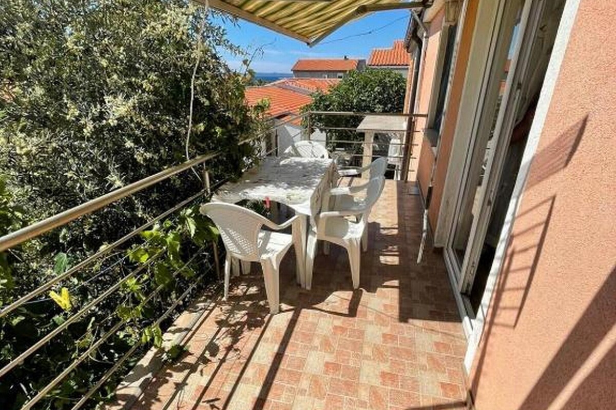 A balcony with a tiled floor, white plastic chairs, a table, and a striped awning.