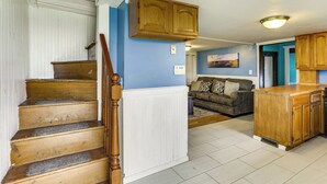 Eine Treppe mit Holzdielen und einem Geländer, ein Wohnzimmer mit einer Couch und einem Gemälde sowie eine Küchenzeile mit Holzschränken und einer Arbeitsplatte.