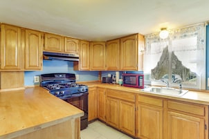 Una cocina con armarios de madera, estufa, microondas y pileta.