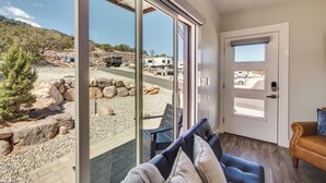 Een modern interieur met een grote schuifglazen deur die uitkomt op een buitenruimte met een rotsachtig landschap en geparkeerde voertuigen.