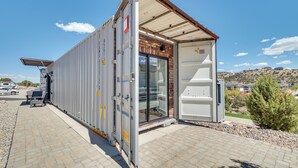 Een modulaire constructie met een glazen deuropening, een metalen dak en een verhard gebied met een geparkeerd voertuig.