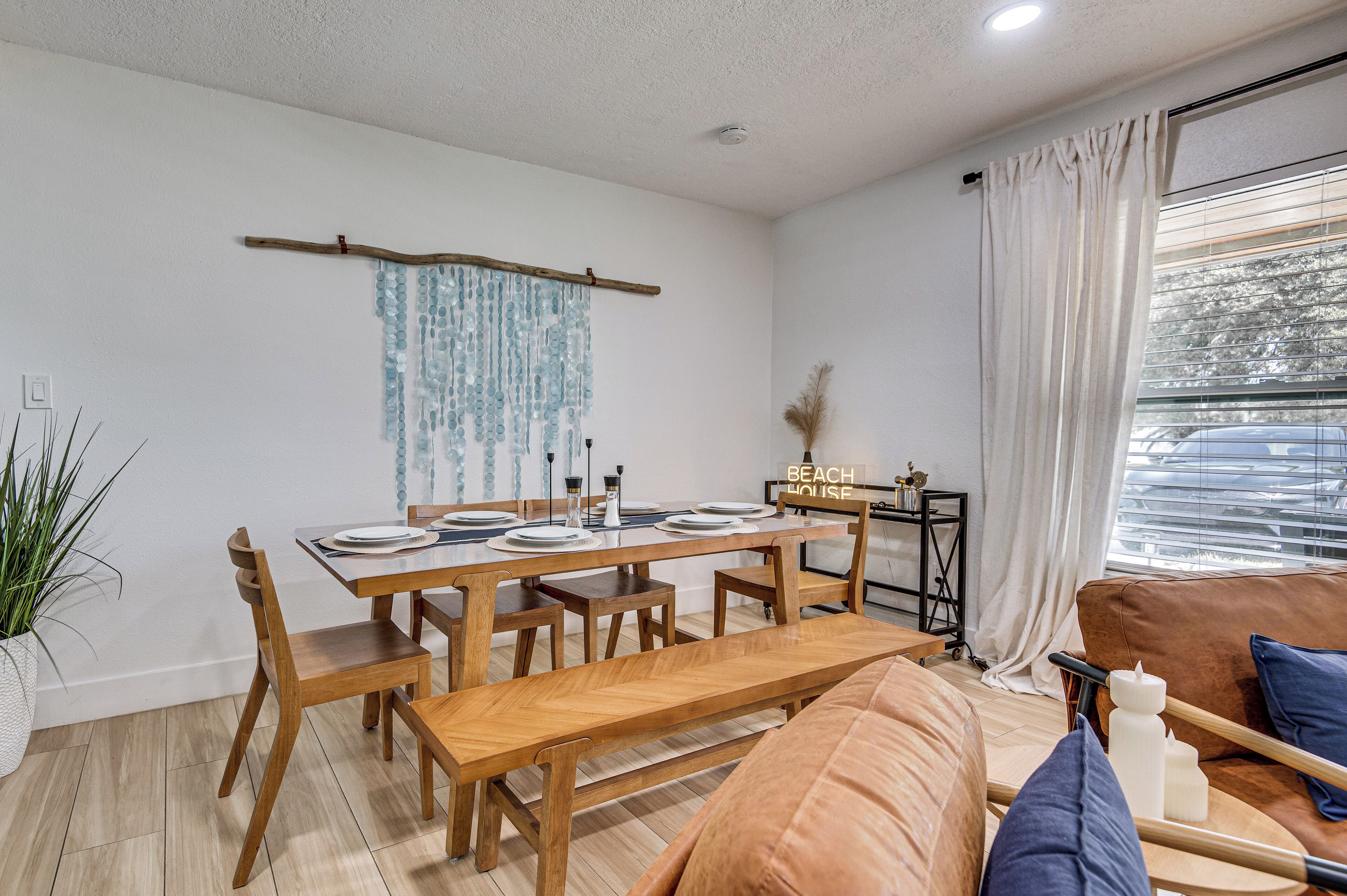 A modern living room with a wooden dining table, benches, a sofa, and a window with curtains.