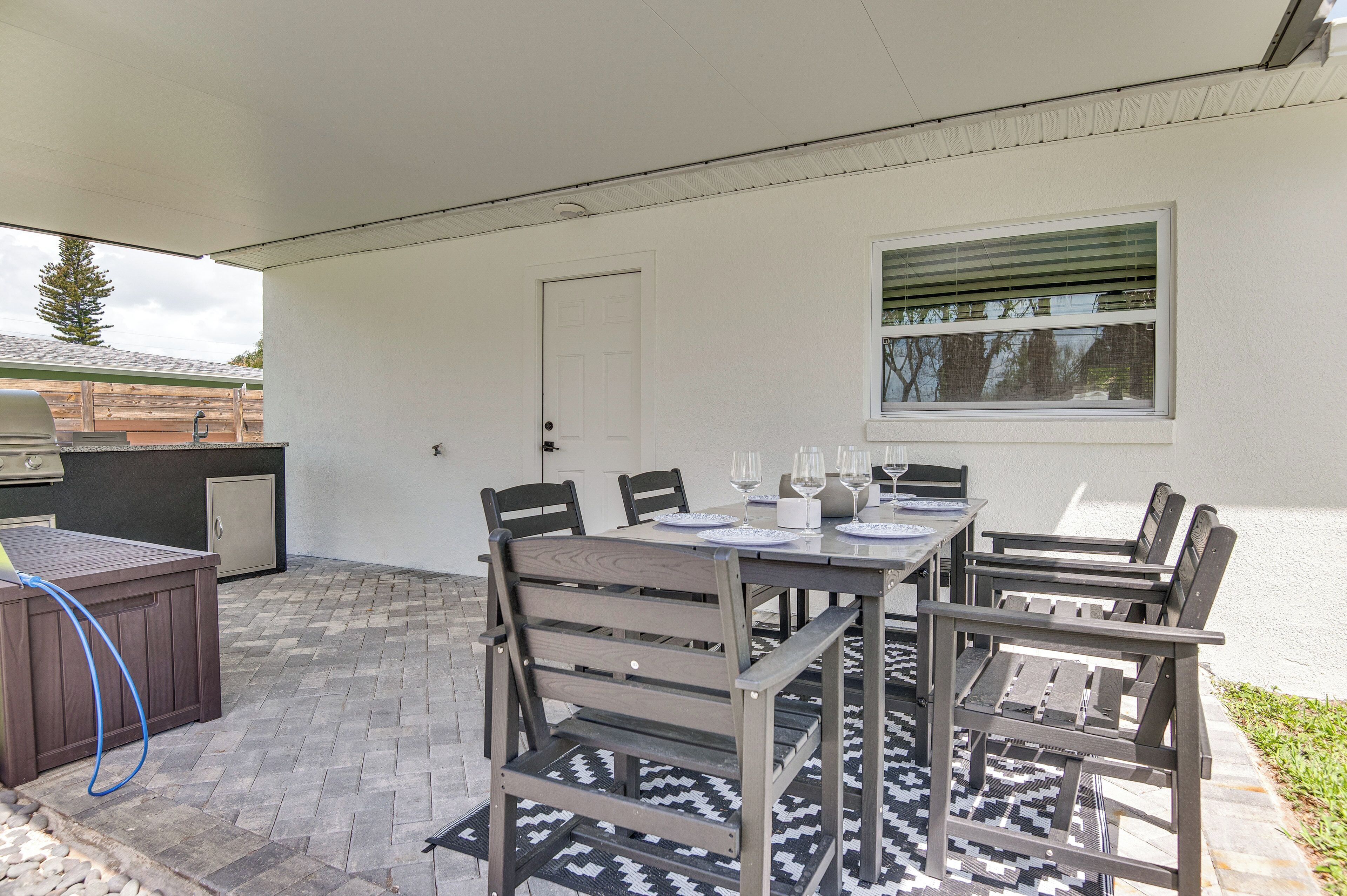 Un patio al aire libre con una mesa lista para cuatro, una parrilla y un área cubierta.