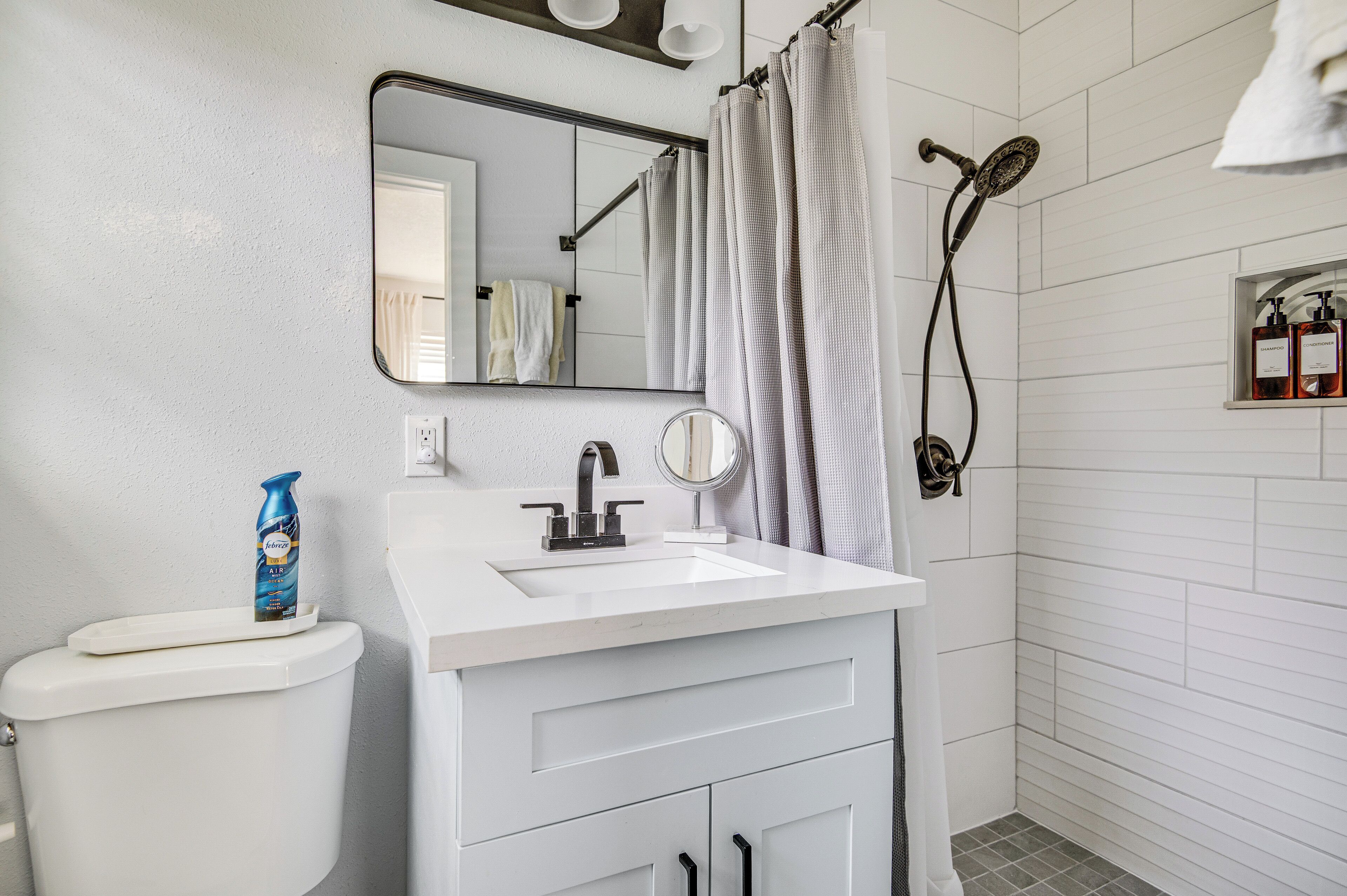 A bathroom with a white sink, a mirror, a toilet, a shower, and a towel rack.