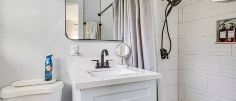 A bathroom with a white sink, a mirror, a toilet, a shower, and a towel rack.