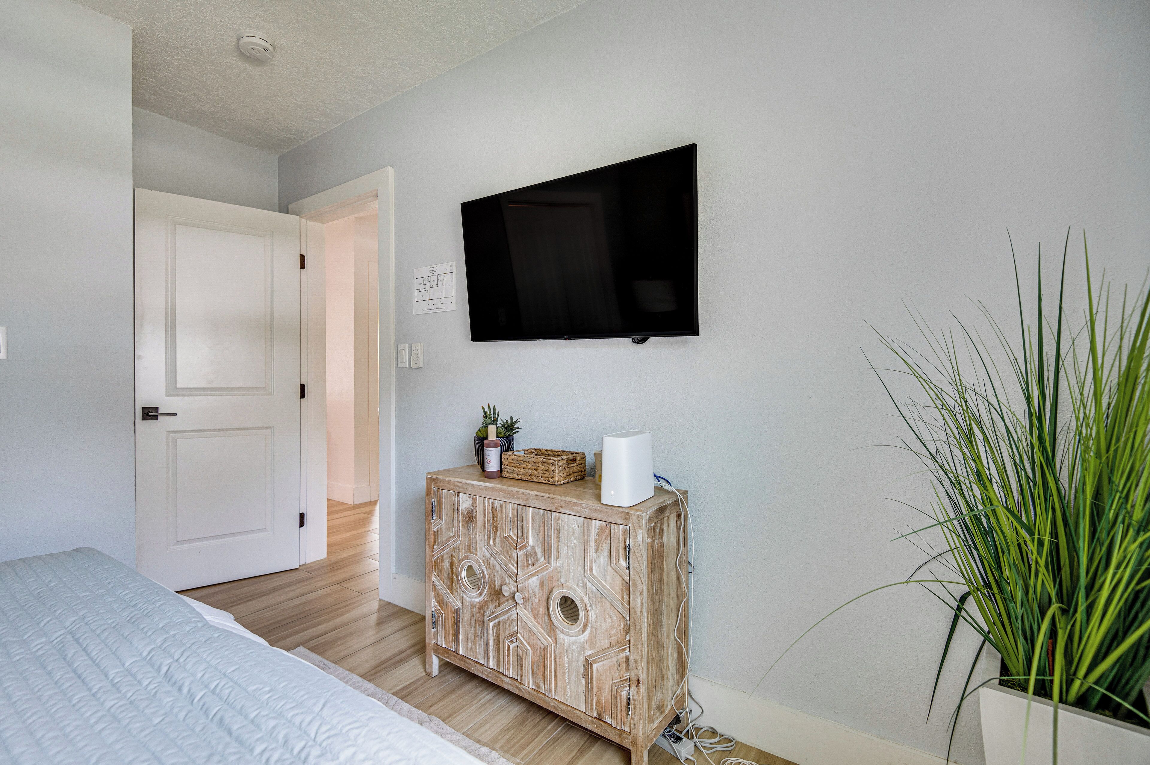 A bedroom with a bed, a wooden cabinet, a flat-screen TV, and a potted plant.