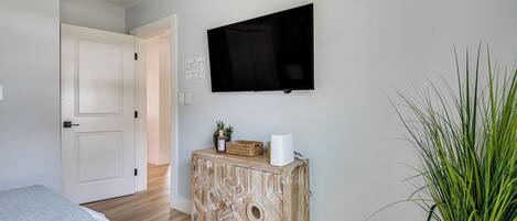 A bedroom with a bed, a wooden cabinet, a flat-screen TV, and a potted plant.