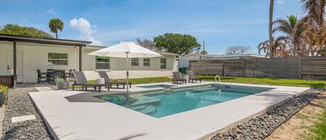 A swimming pool with lounge chairs, a covered patio, and a house in the background.