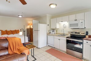 Cocina compacta con armarios blancos, microondas, estufa y lavavajillas.
