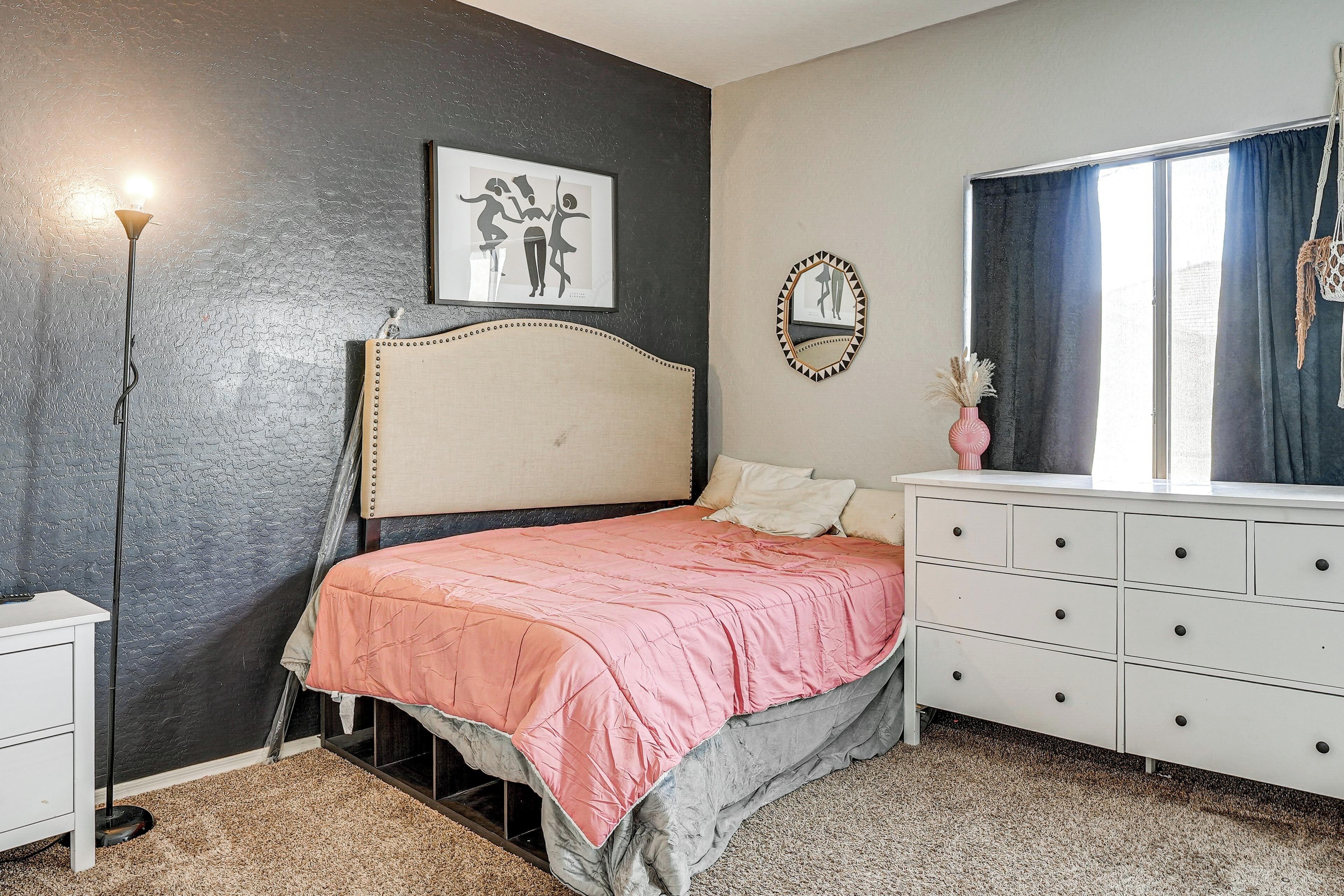 Un dormitorio con cama, cómoda, mesita de noche y una pared decorada con un cuadro enmarcado.