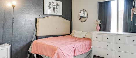 Un dormitorio con cama, cómoda, mesita de noche y una pared decorada con un cuadro enmarcado.