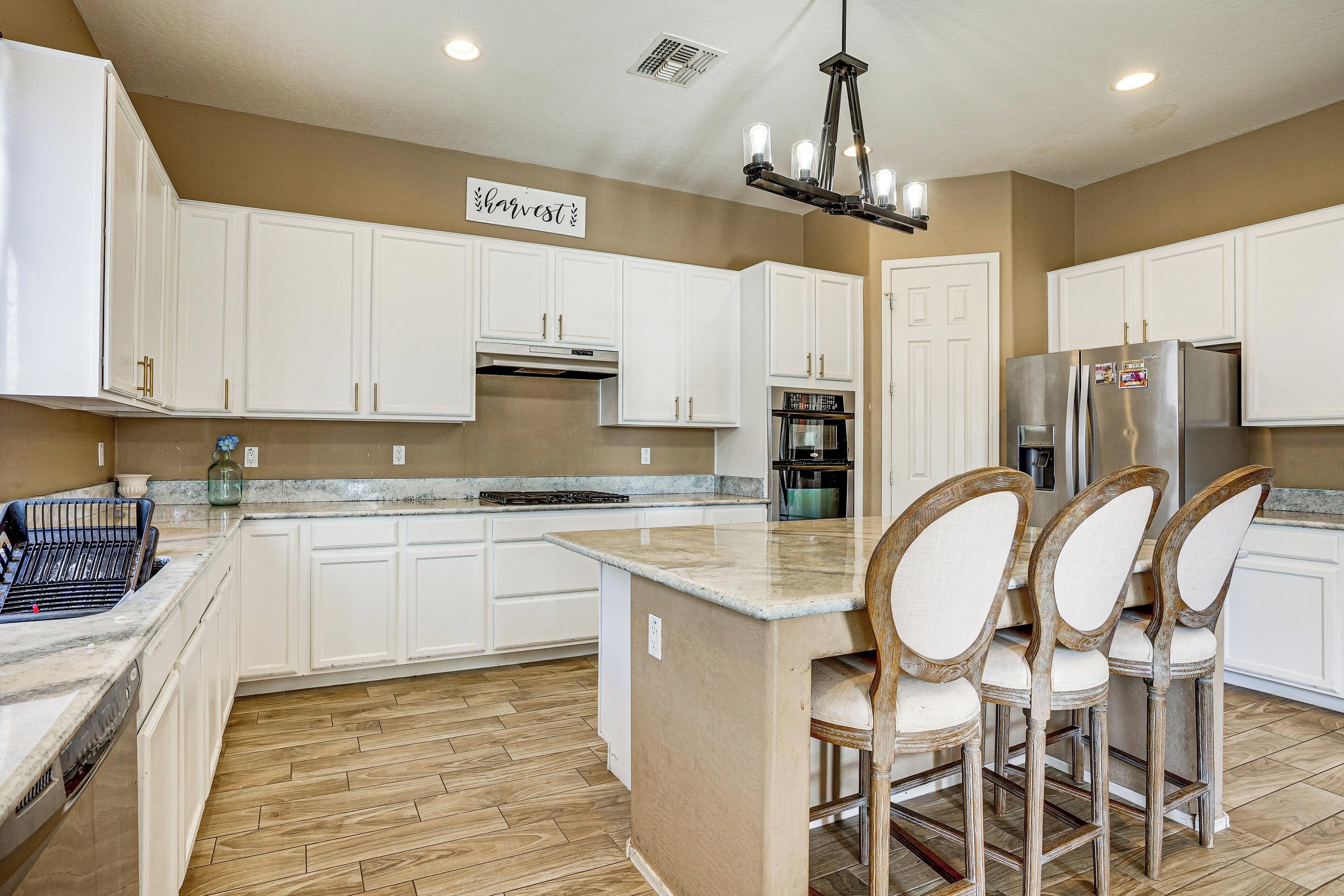A kitchen with white cabinets, a central island, bar stools, a stainless steel refrigerator, and a chandelier.