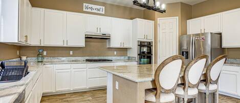A kitchen with white cabinets, a central island, bar stools, a stainless steel refrigerator, and a chandelier.