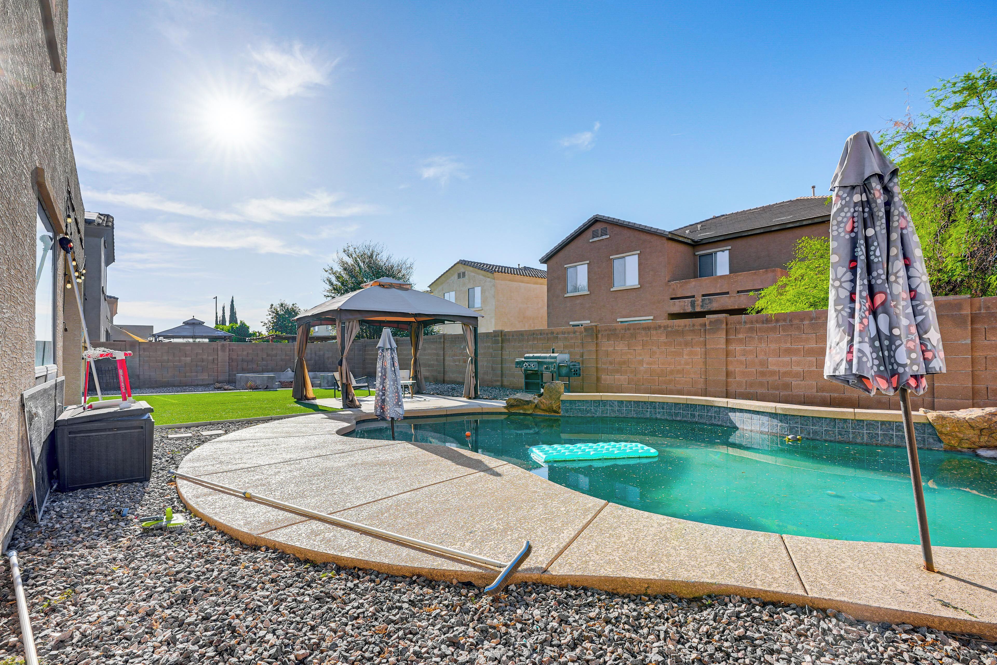 A backyard with a swimming pool, a patio area, and a covered seating area.
