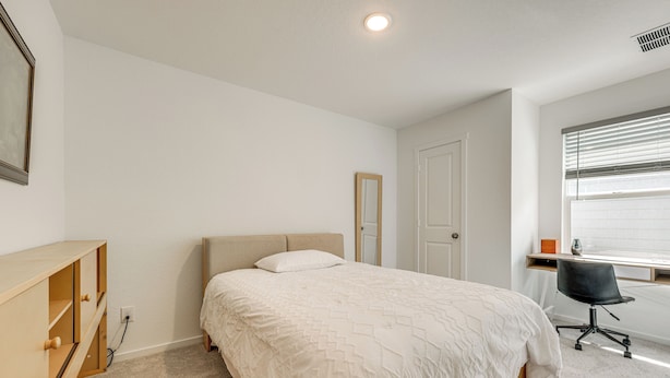 Une chambre à coucher comprenant un lit, un bureau, une chaise, une armoire et une fenêtre avec des stores.