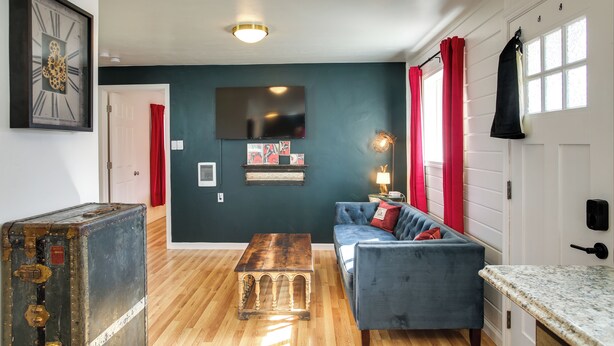 A living room with a blue sofa, a wooden coffee table, a vintage suitcase, a flat-screen TV, and a red curtain. - Unit 8: Our Largest & Highest-rated 1-br (Spokane)