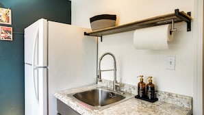 A kitchen with a stainless steel sink, a white refrigerator, a wooden shelf with a basket, and two soap dispensers. - Unit 8: Our Largest & Highest-rated 1-br (Spokane)