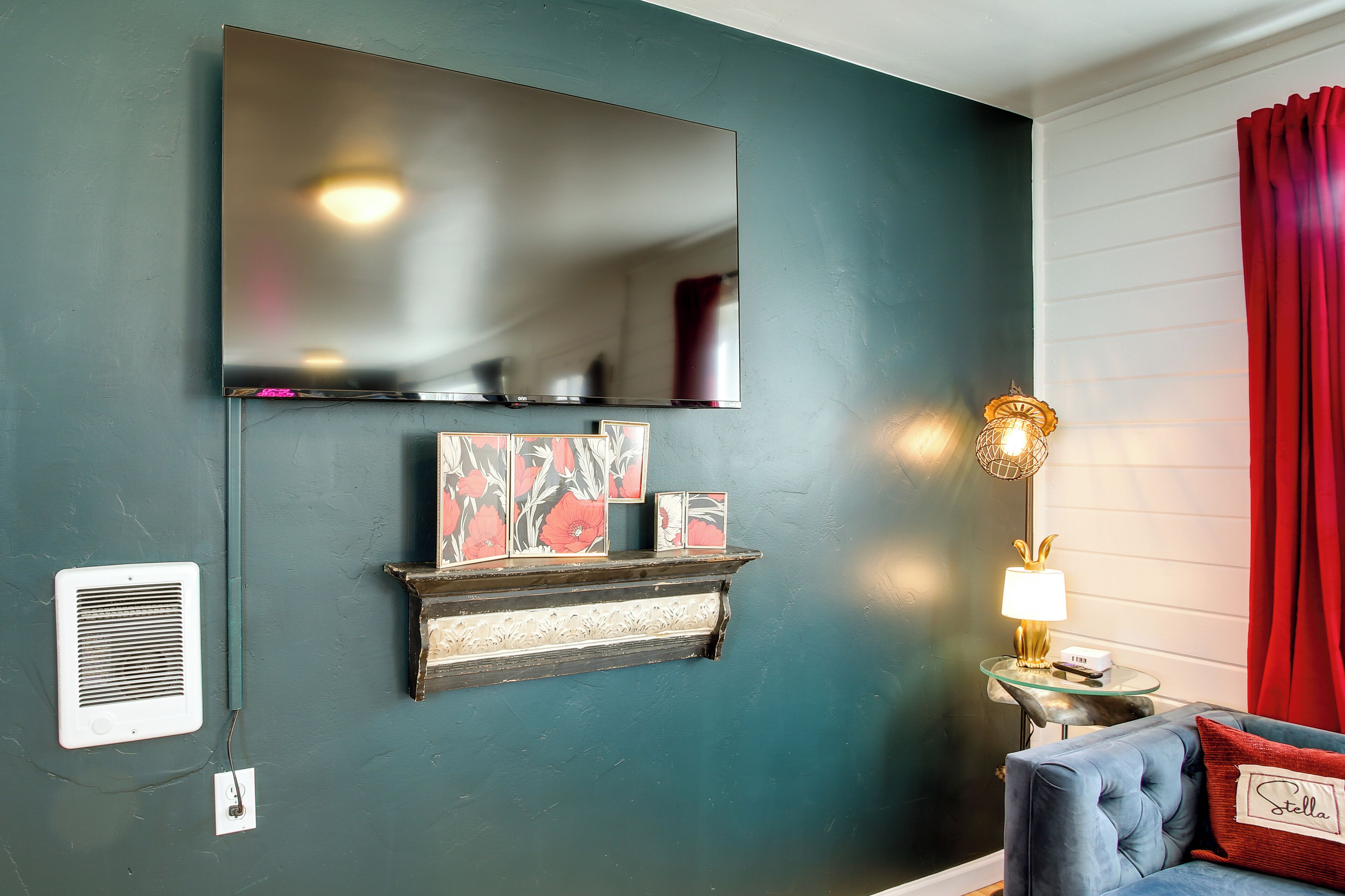 A room with a large mirror, a fireplace with decorative items, a red curtain, and a lamp on a side table.