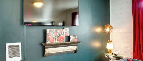 A room with a large mirror, a fireplace with decorative items, a red curtain, and a lamp on a side table.