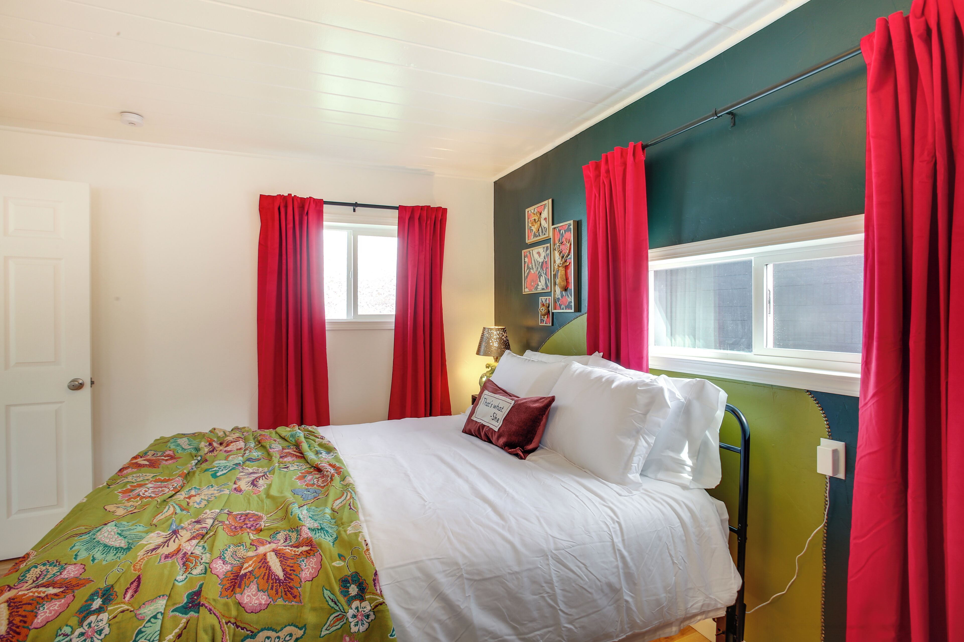 A bedroom with a bed, red curtains, a green wall, and a window.